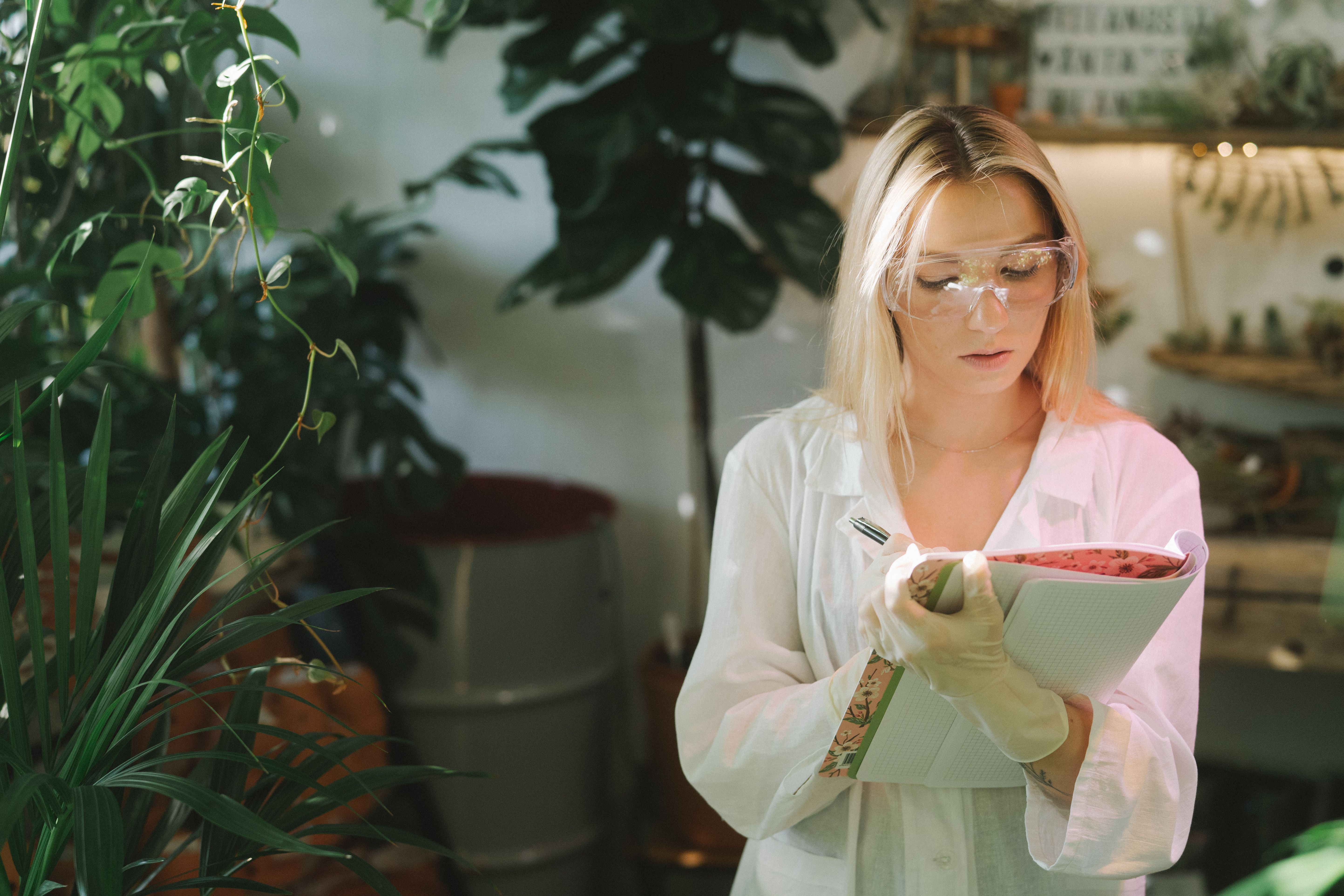 Focused botanist writing down plant care observations in a notebook surrounded by plants